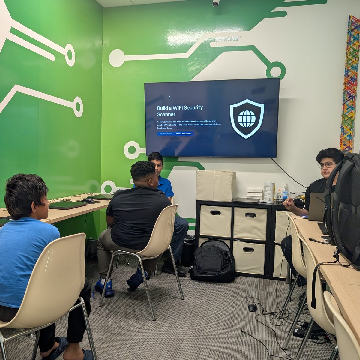 Students at a Cybersentinelz workshop watching a screen that reads “Build a WiFi Security Scanner” while a student instructor leads the session